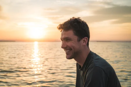 A man smiling against a scenic sunset at sea