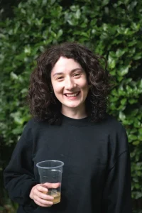 Woman with dark curly hair holding a drink in a plastic cup smiling